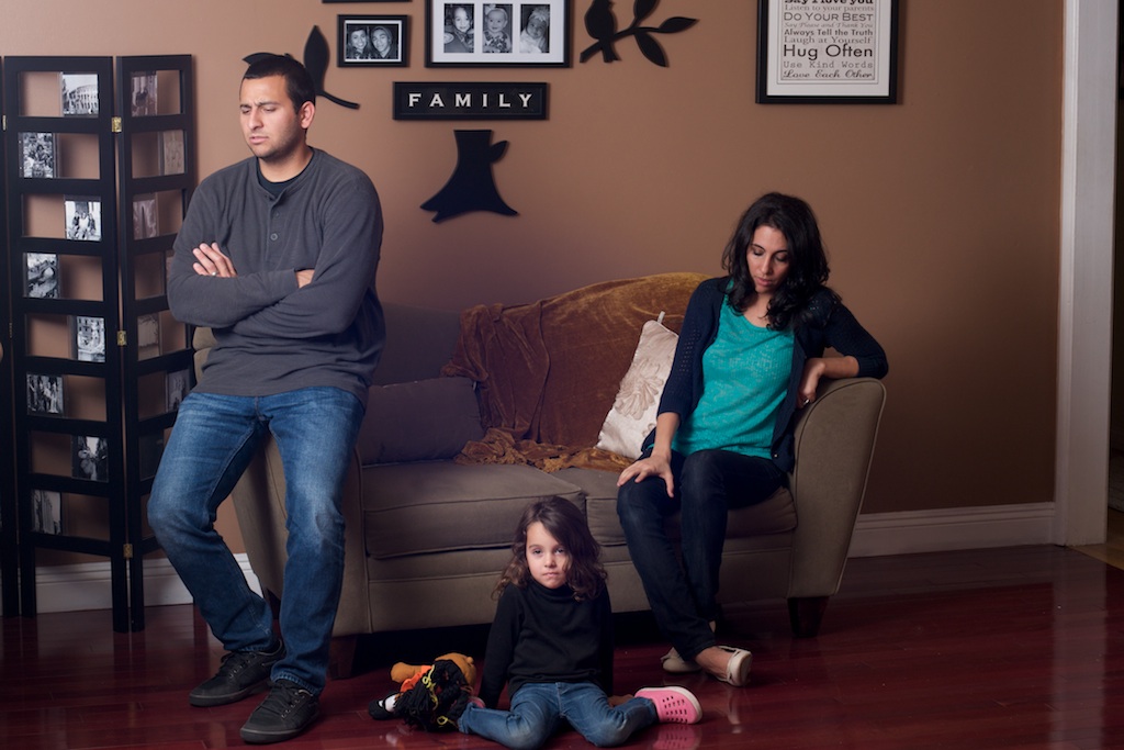 husband and wife is sitting on a couch while their daughter is sitting on floor and are offended.